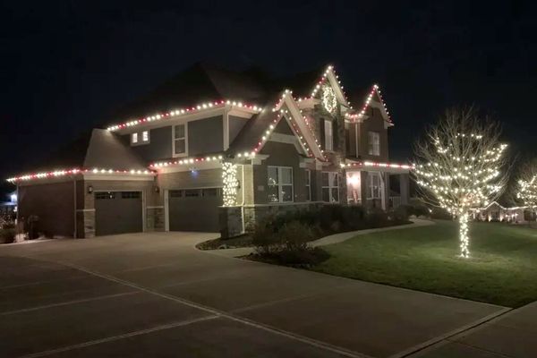 Red and white Christmas lights on the roofline of a two-story home with a wrapped tree in Blue Ash, OH