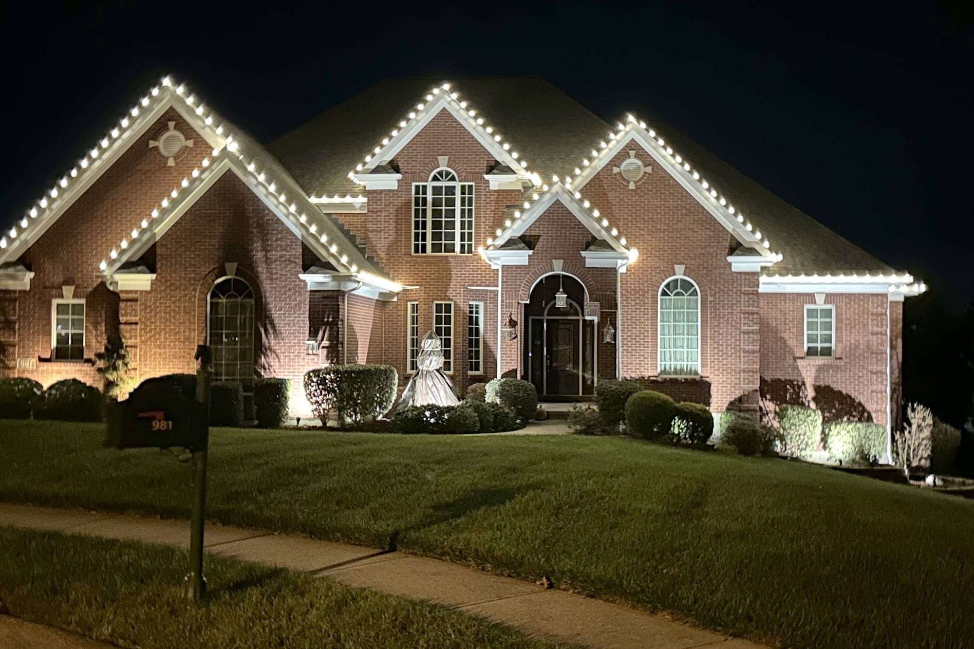 Brick home with warm white C9 Christmas lights outlining every roofline peak at night, installed by Liberty Christmas Lights