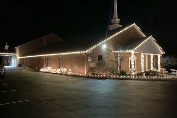 Church with warm white Christmas lights outlining the roofline and entry at night