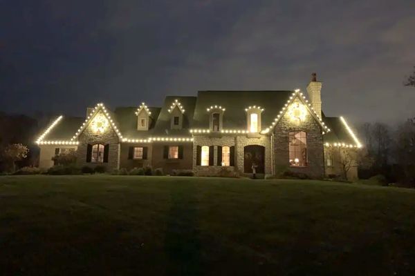 Warm white C9 Christmas lights along the roofline and dormers of a stone home in Cincinnati, OH