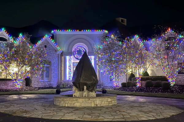 Large stone estate with multicolor roofline lights and lit trees around a circular drive