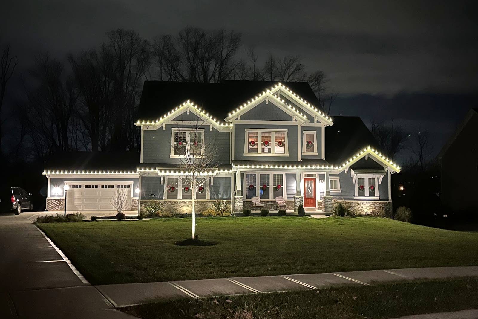 Gray two-story home with warm white Christmas lights along the roofline and garage at night, installed by Liberty Christmas Lights
