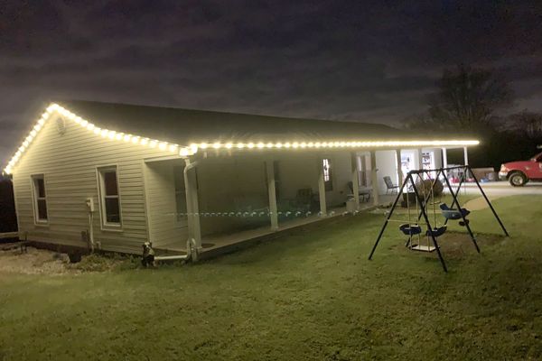 Ranch home with warm white Christmas lights along a long roofline and covered porch
