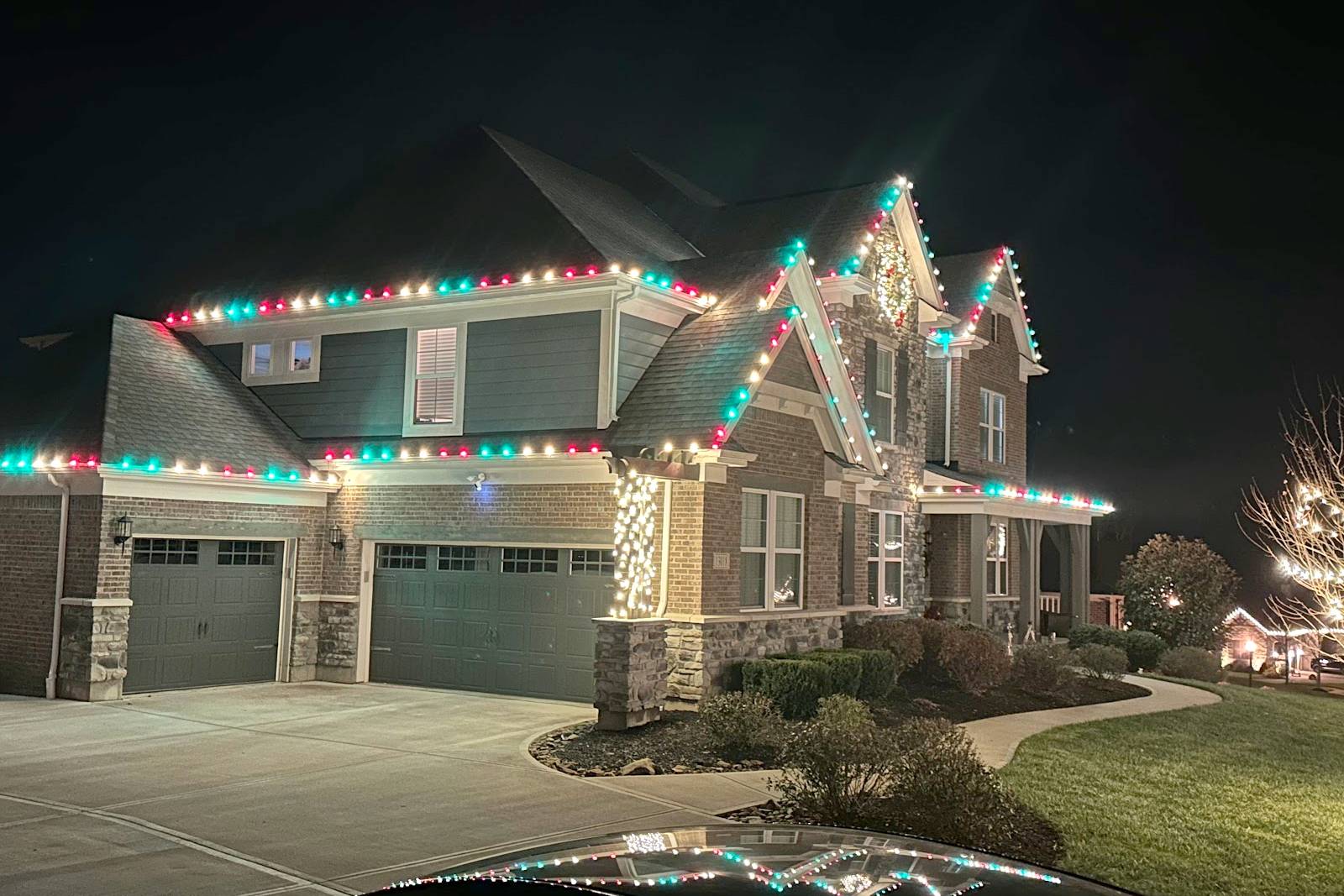 Two-story home with red, green, and white C9 Christmas lights along the roofline, installed by Liberty Christmas Lights
