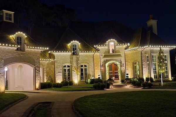 Stone estate with warm white Christmas lights on the roofline, dormers, and windows