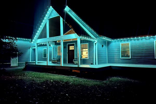 Home with teal Christmas lights along the gables and porch roof at night