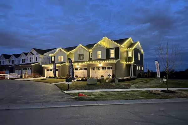 Row of townhomes with warm white Christmas lights on every roof peak at dusk
