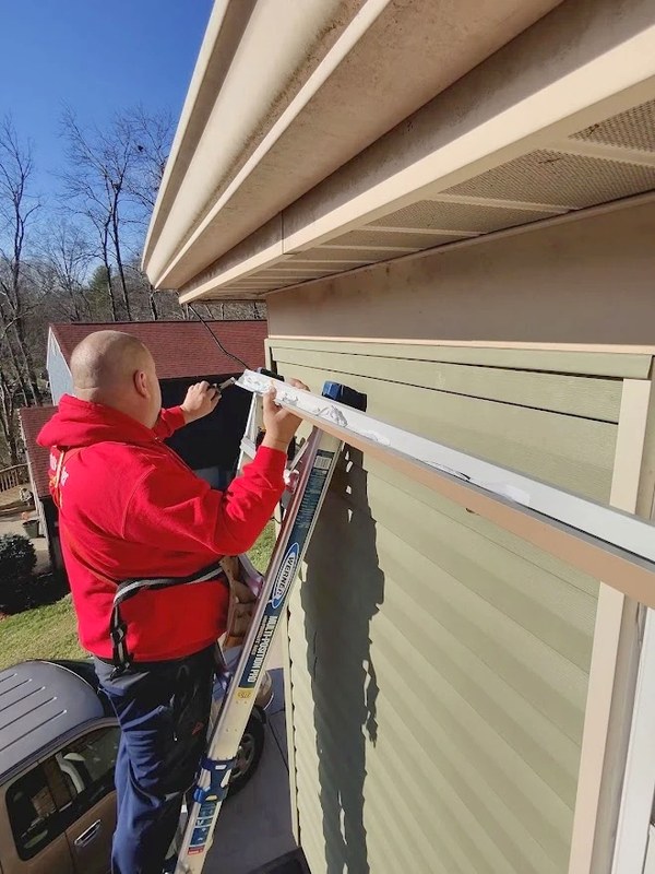 DJ, owner of Liberty Christmas Lights, on a ladder clipping Christmas lights along a roofline