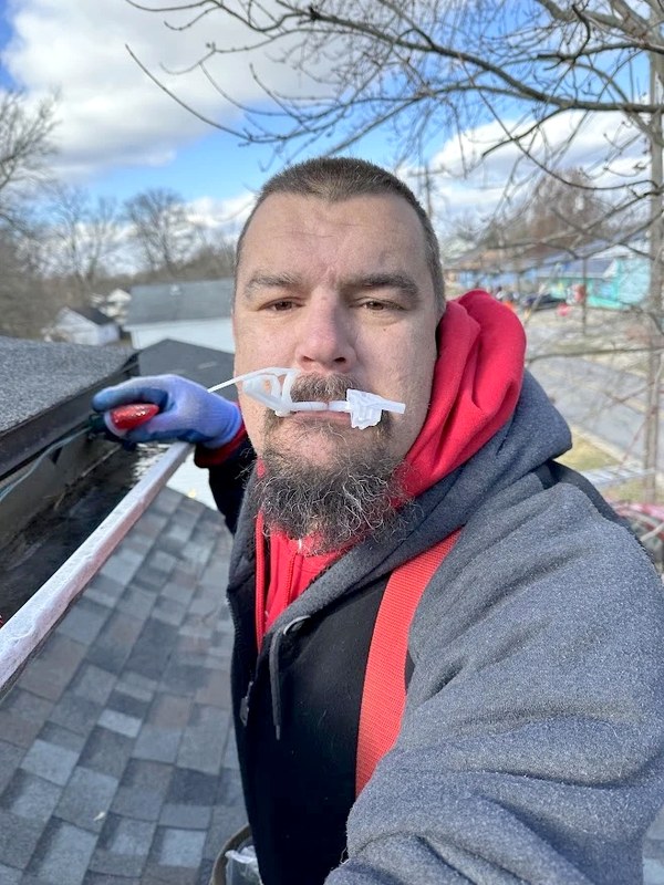DJ on a roof mid-install, holding a light clip in his teeth