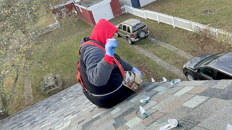 DJ in a safety harness clipping C9 lights along a roof edge